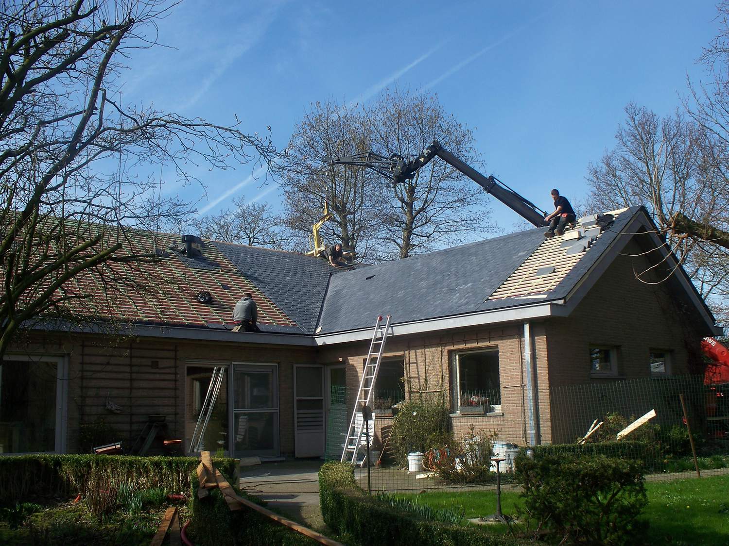 Dakwerkers aan het werk op een hellend dak, met een mobiele kraan